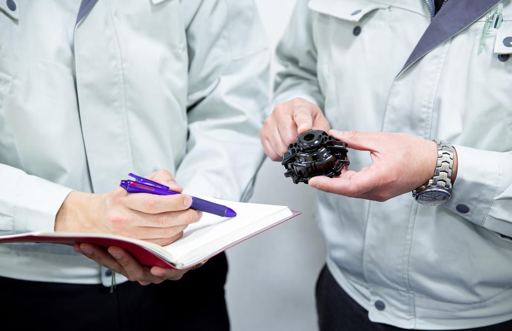 樹脂自動車部品を手にして話をする二人の人物