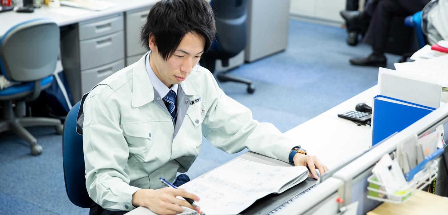 デスクで部品の手配などの事務仕事をしている様子